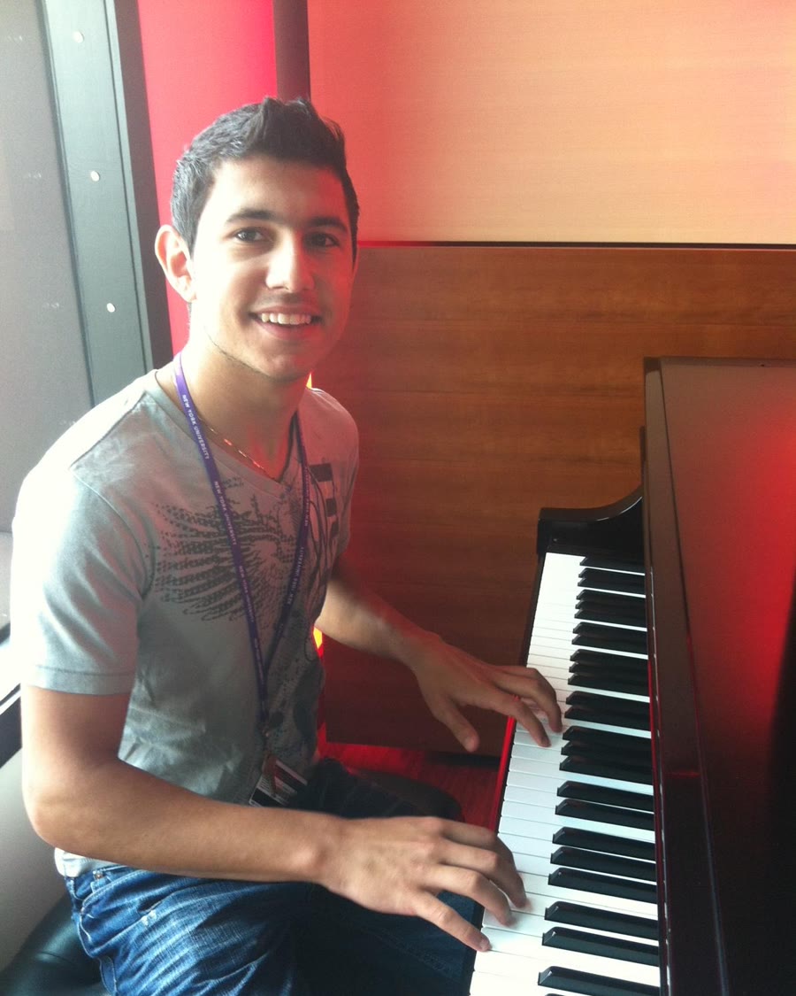 Paul at a piano at NYU, wearing a university lanyard